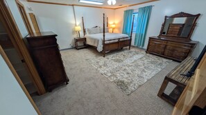 Une chambre à coucher avec un lit à baldaquin, une commode, un miroir et un sol recouvert d’une moquette.