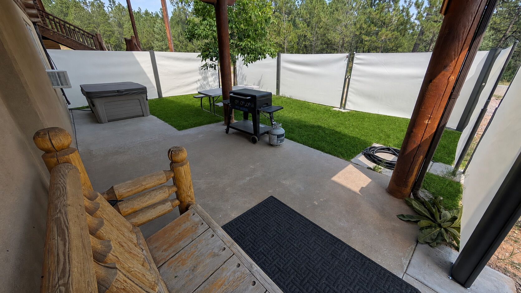 A patio with a wooden bench, a grill, and a small table.