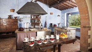 Une cuisine rustique avec un mur en briques, des armoires en bois et un grand îlot central où sont disposés des aliments pour le petit-déjeuner.