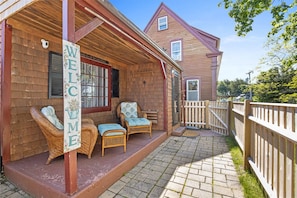 A wooden house with a porch, two wicker chairs, and a welcome sign.