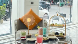 A modern hotel lobby with a marble floor, a sofa with a decorative pillow, a glass table with a drink and snacks, and a view of the street through large windows. - SC Luxury Hotel (Bai Chay)