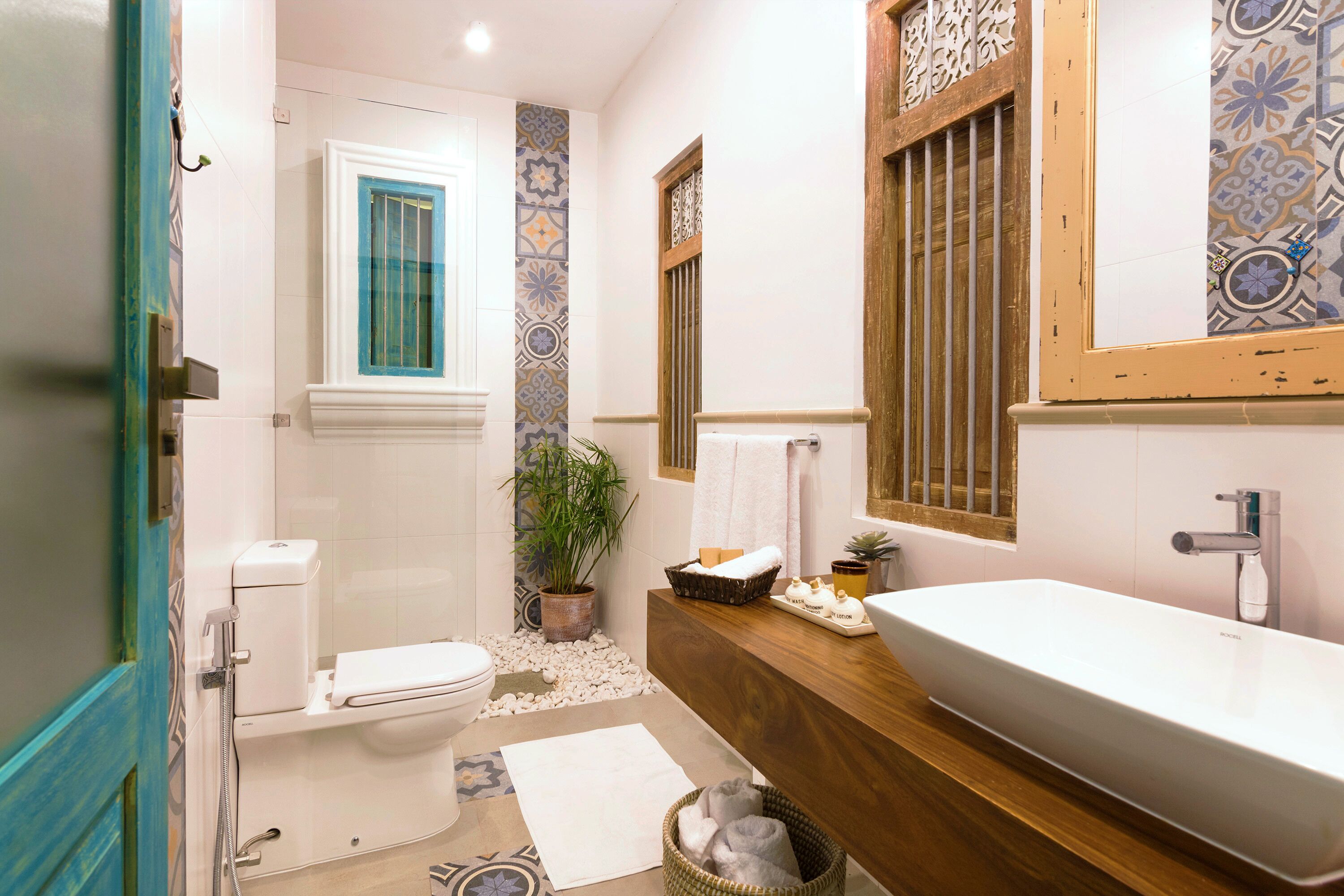 Ein Badezimmer mit Toilette, Waschbecken, Spiegel und einem Fenster mit blauem Rahmen.