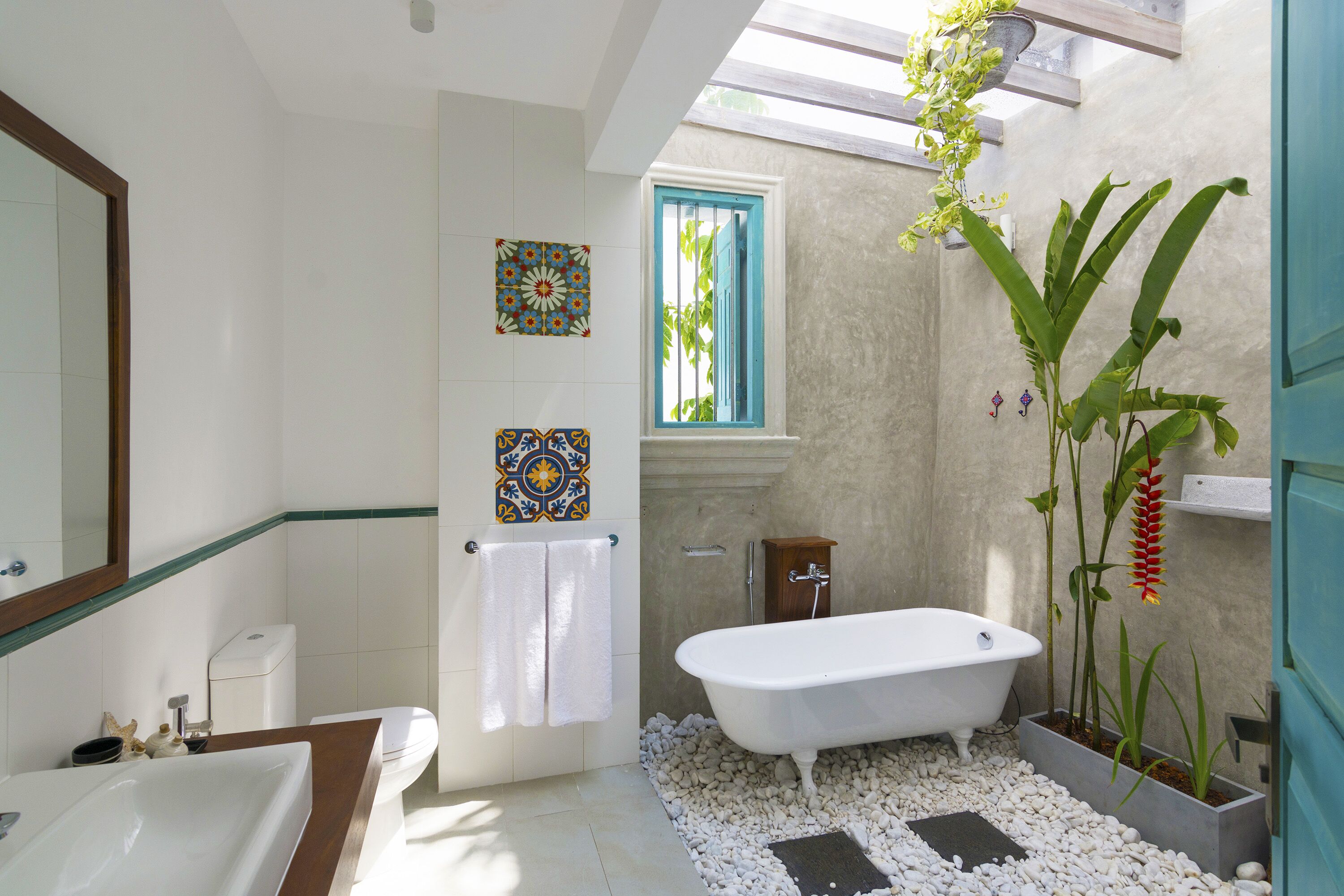 A bathroom with a bathtub, white tiles, a window with blue shutters, and decorative tiles on the wall.