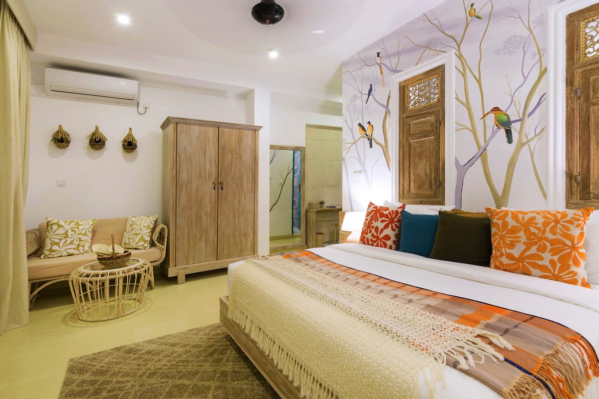 A bedroom with a large bed, a wooden wardrobe, a sofa, and a small round table.