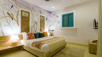 A bedroom with a bed, nightstands, a lamp, a window with blue shutters, and wall art of birds on trees.