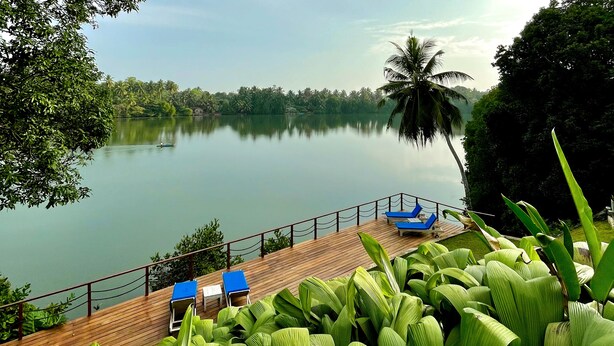 A wooden deck with lounge chairs overlooking a calm lake, surrounded by lush greenery and palm trees. - 33 Lake Terrace  (Hikkaduwa)
