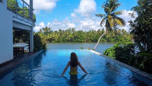 A woman in a pool with a view of a lake and palm trees. - 33 Lake Terrace  (Hikkaduwa)