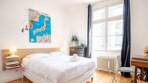 Siististi järjestetty hotellihuone, jossa on suuri sänky, yöpöydät lamppuineen, seinällä oleva kartta, ikkuna verhoineen sekä pieni työpöytä tuolilla.
