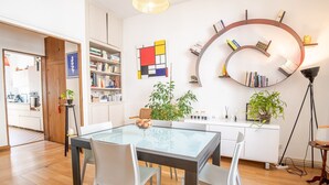 Moderni keittiö, jossa on valkoiset kaapit, ruokapöytä tuoleineen ja kirjahylly täynnä kirjoja.