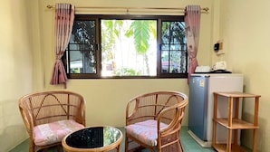 Una habitación con dos sillas de mimbre, una mesita, un refrigerador y una estantería.