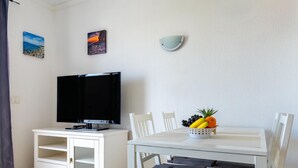 A room with a flat-screen TV, a dining table with chairs, a fruit basket, and two wall-mounted paintings. - Port Royale shine and bright, heated pool (Los Cristianos)