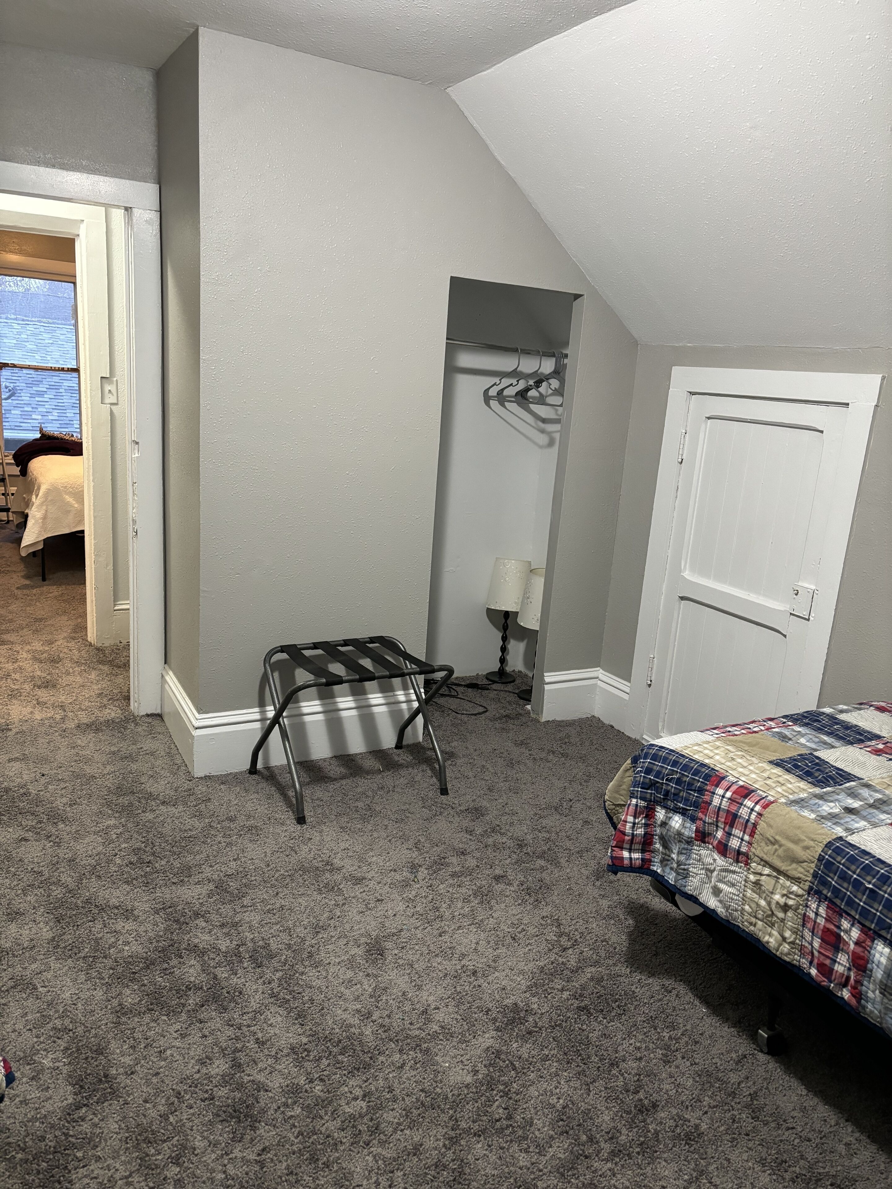 Un dormitorio con cama, una silla, un armario y una puerta.