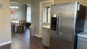 Una cocina con un refrigerador de acero inoxidable, una mesa de comedor con sillas y un bote de basura.