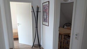Een gang met een prullenbak, een schilderij en een eetgedeelte met een tafel en stoelen.