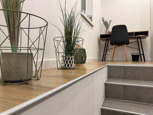 Un interior moderno con una escalera, un escritorio y dos plantas en macetas.