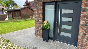 Ein modernes Gebäude mit einer dunkelgrauen Tür, einer Ziegelwand und einem kleinen Blumenkasten mit gelben Blumen.