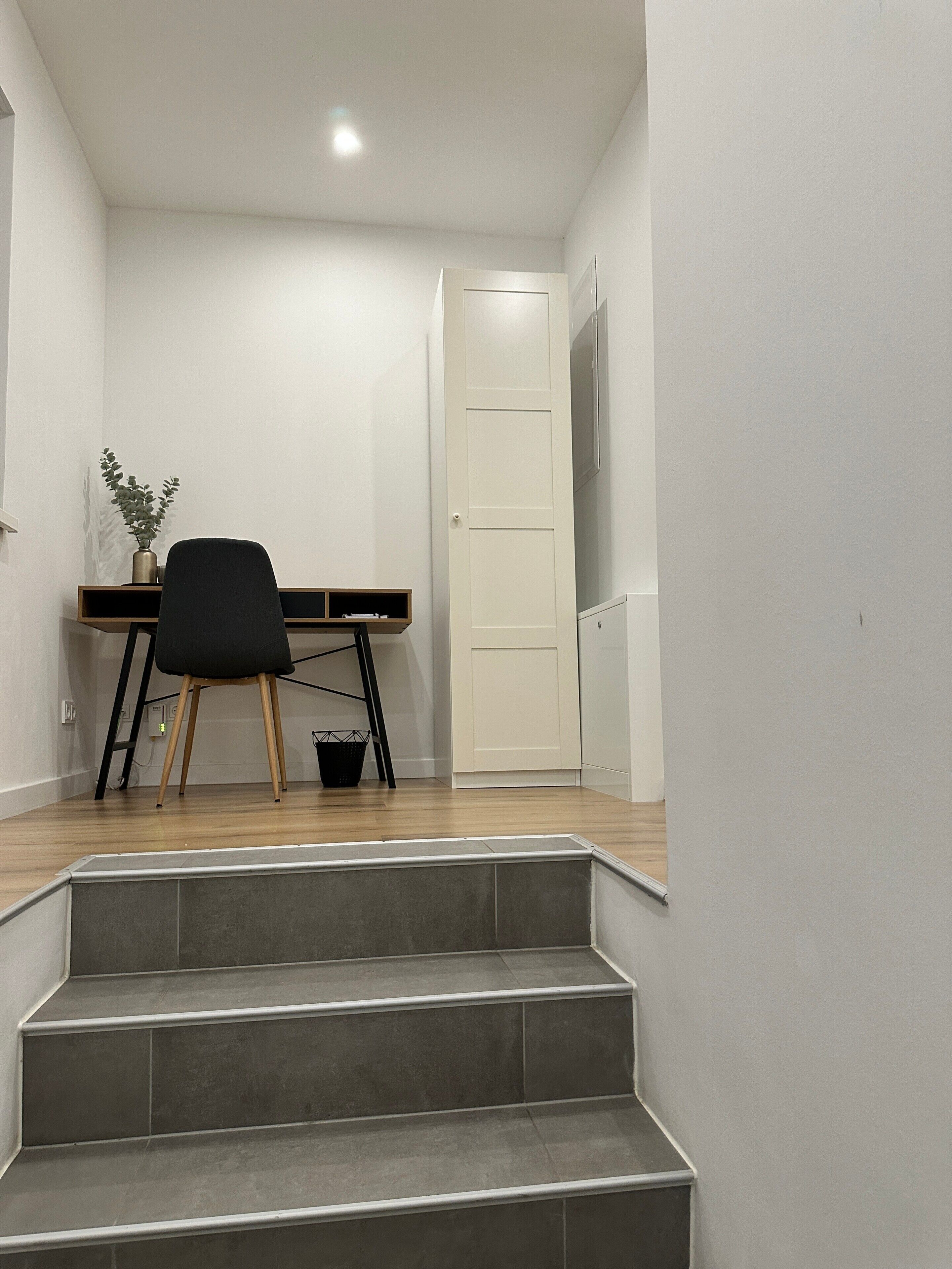 Un escalier menant à une pièce où se trouvent un bureau, une chaise et une plante en pot.