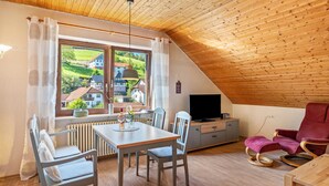 Een eethoek met een tafel, stoelen, een televisie en een rode fauteuil.