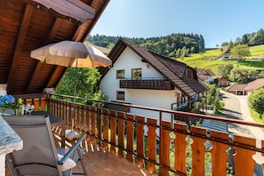 Un balcon avec une balustrade en bois, une table avec des chaises et une vue sur une maison blanche dotée d’un balcon.
