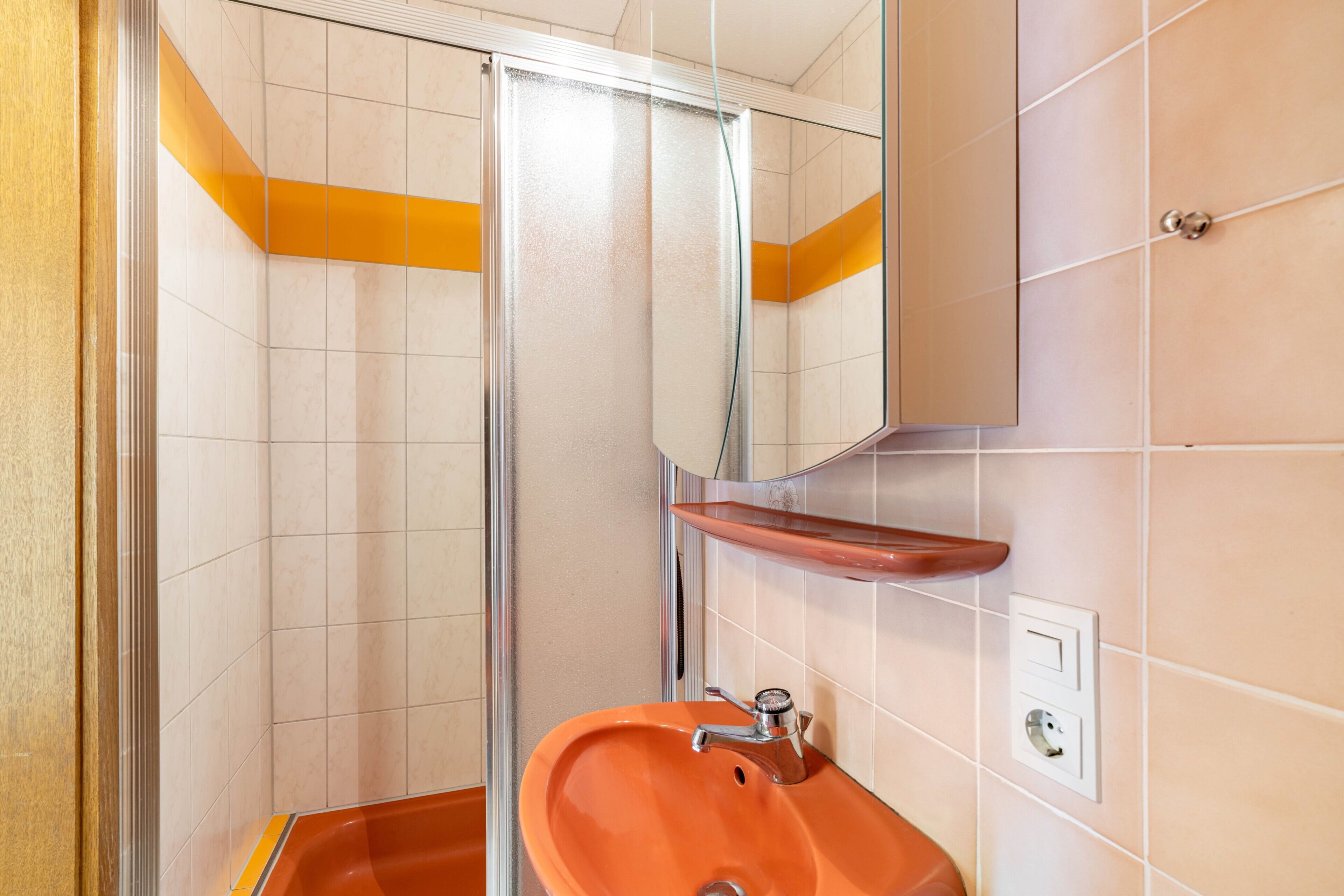 A bathroom with a glass shower enclosure, a sink with a faucet, and a mirror on the wall.