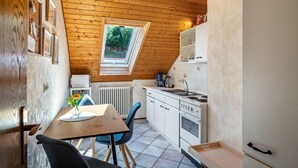 Een compacte keuken met een houten plafond, dakraam, witte kastjes en een eethoek met tafel en stoelen.