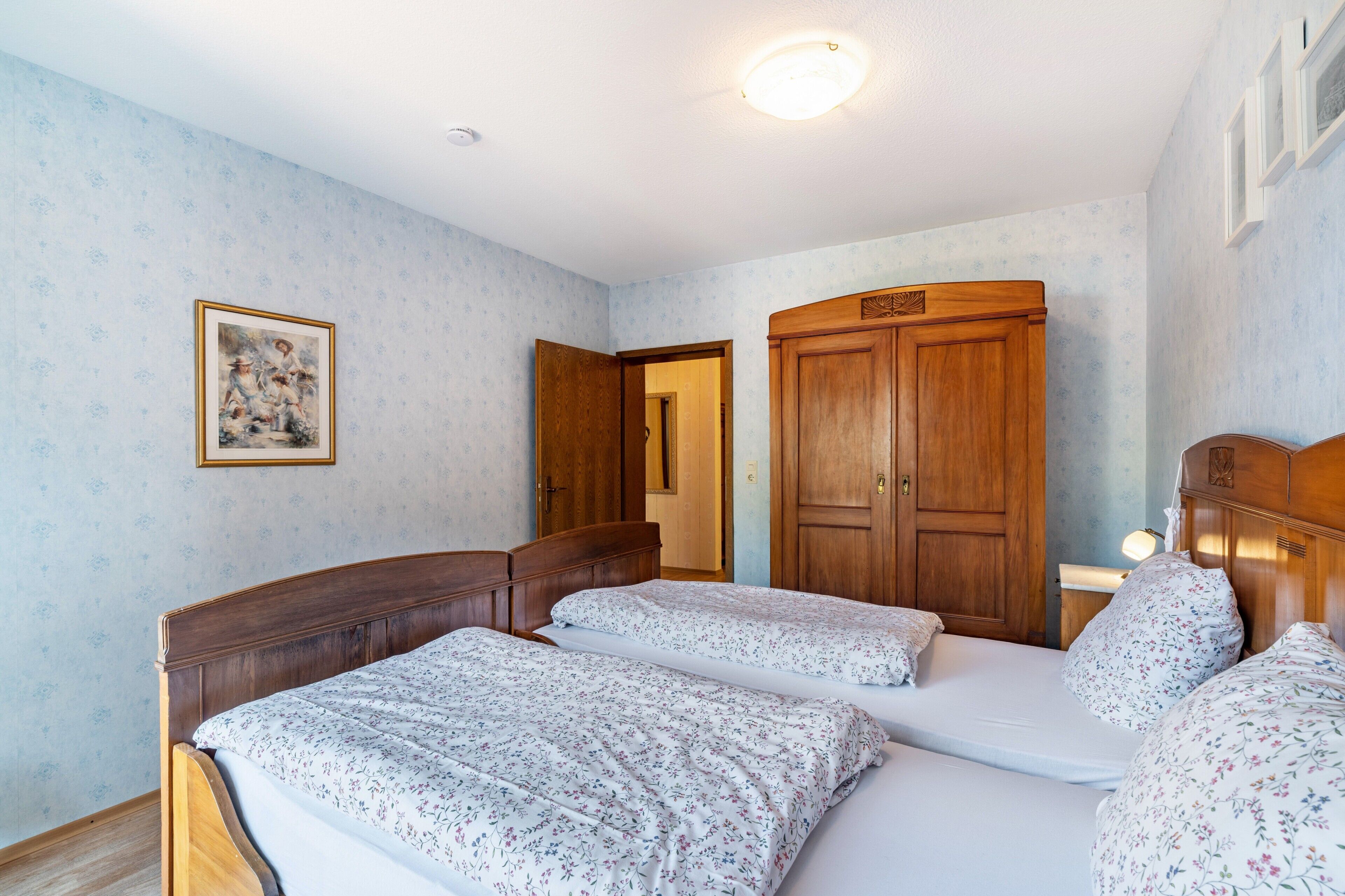 A bedroom with two beds, wooden wardrobe, and a framed picture on the wall.