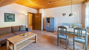 Een gezellige zithoek met houten plafond, een bank, een salontafel, een eettafel met stoelen en een kast.