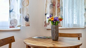 A wooden table with a vase of flowers, a chair, and a window with curtains. - Studio Apartment ' In der Stadt und Natur' with Wi-Fi (Calw)