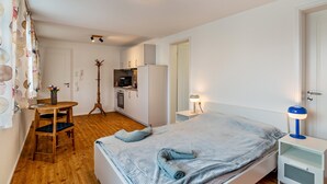 A bedroom with a bed, bedside table, lamp, and a small kitchenette in the background. - Studio Apartment ' In der Stadt und Natur' with Wi-Fi (Calw)