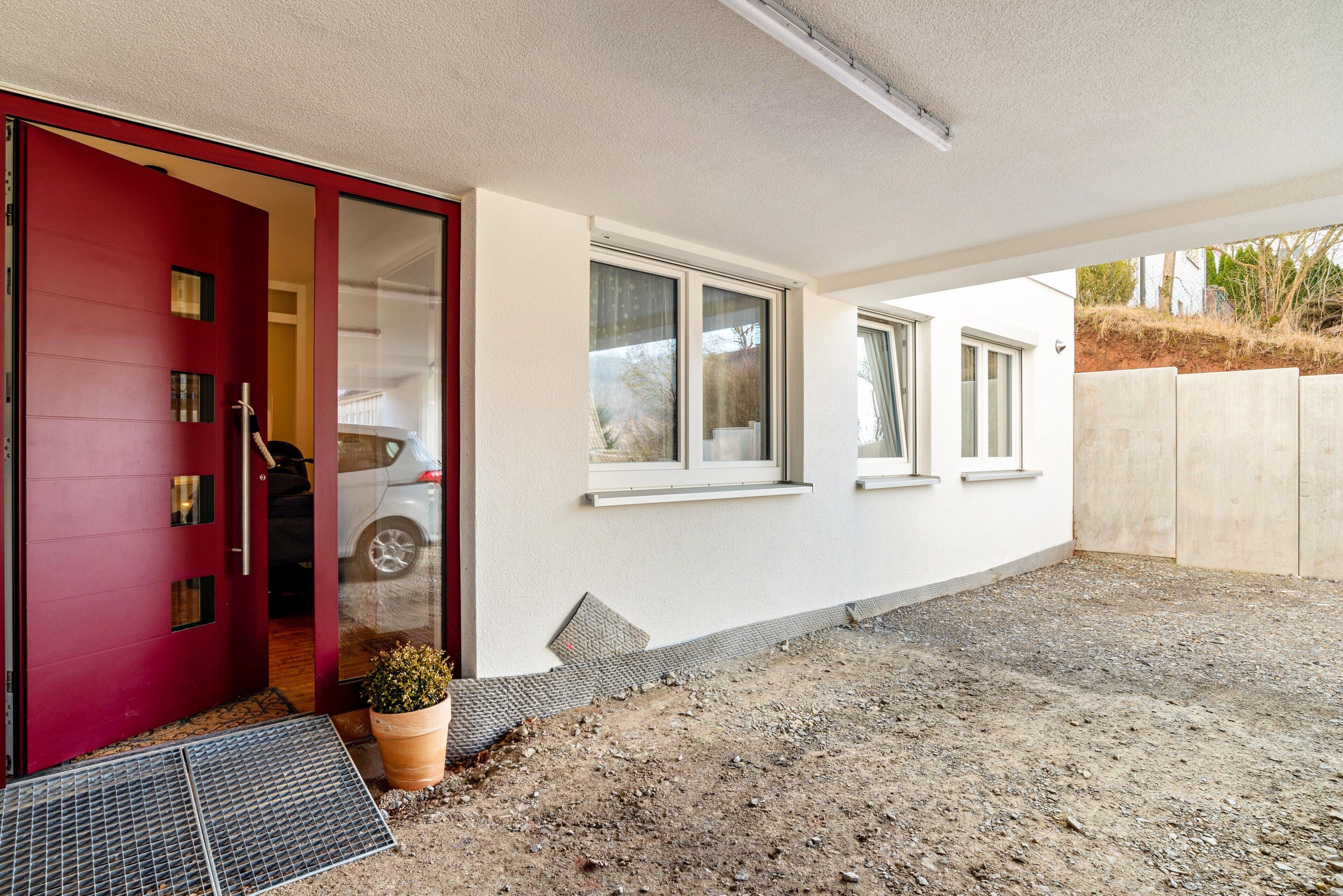 Una casa con puerta roja, fachada blanca y camino de entrada de grava.