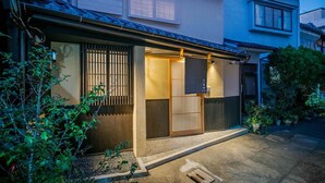 Ein traditionelles japanisches Haus mit einer Schiebetür, einem kleinen Garten und einem gut beleuchteten Eingang.