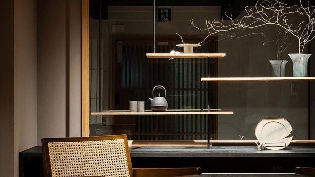 Ein modernes Interieur mit einem Holzstuhl, einem runden Beistelltisch und einem Regal mit Dekoration.