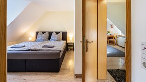 Een slaapkamer met een bed, nachtkastjes en uitzicht op een eetruimte.