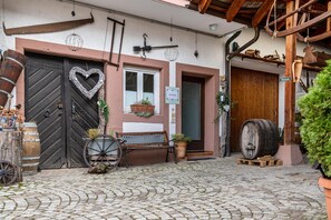 Ein Kopfsteinpflasterhof mit einer hölzernen Bank, einer schwarzen Tür mit Herzmotiv und einem Holzbottich.