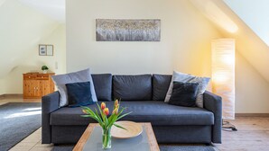Een moderne woonkamer met een grijze bank, een houten salontafel met een bloemenvaas, een schilderij aan de muur en een hoge staande lamp.