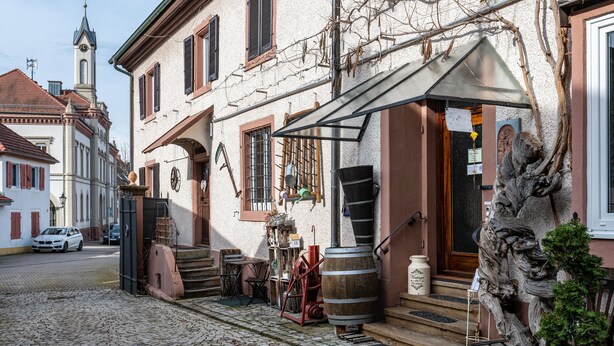 Een geplaveid straatje met een gebouw dat een traditionele gevel, een zichtbare trap en een vat heeft.