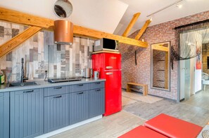Una cocina moderna con armarios grises, un refrigerador rojo y techo de madera.