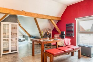 Un comedor con una mesa de madera, bancos rojos, un armario con puertas de cristal, un ventilador y una máquina de café.