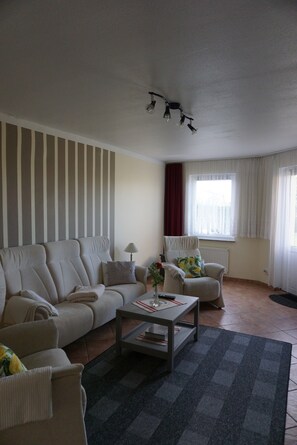 A living room with a sofa, armchair, coffee table, and a window with curtains.