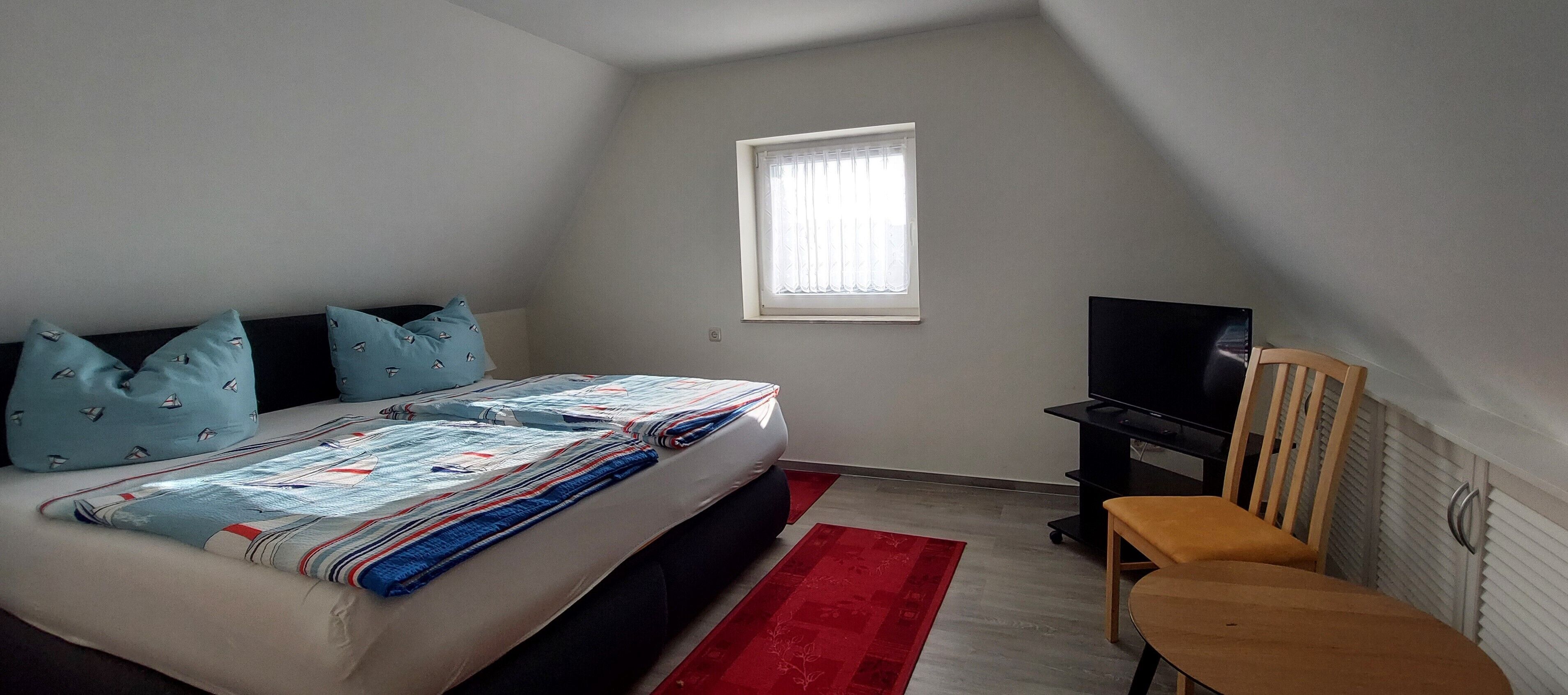 A bedroom with a bed, a television, a chair, and a window.