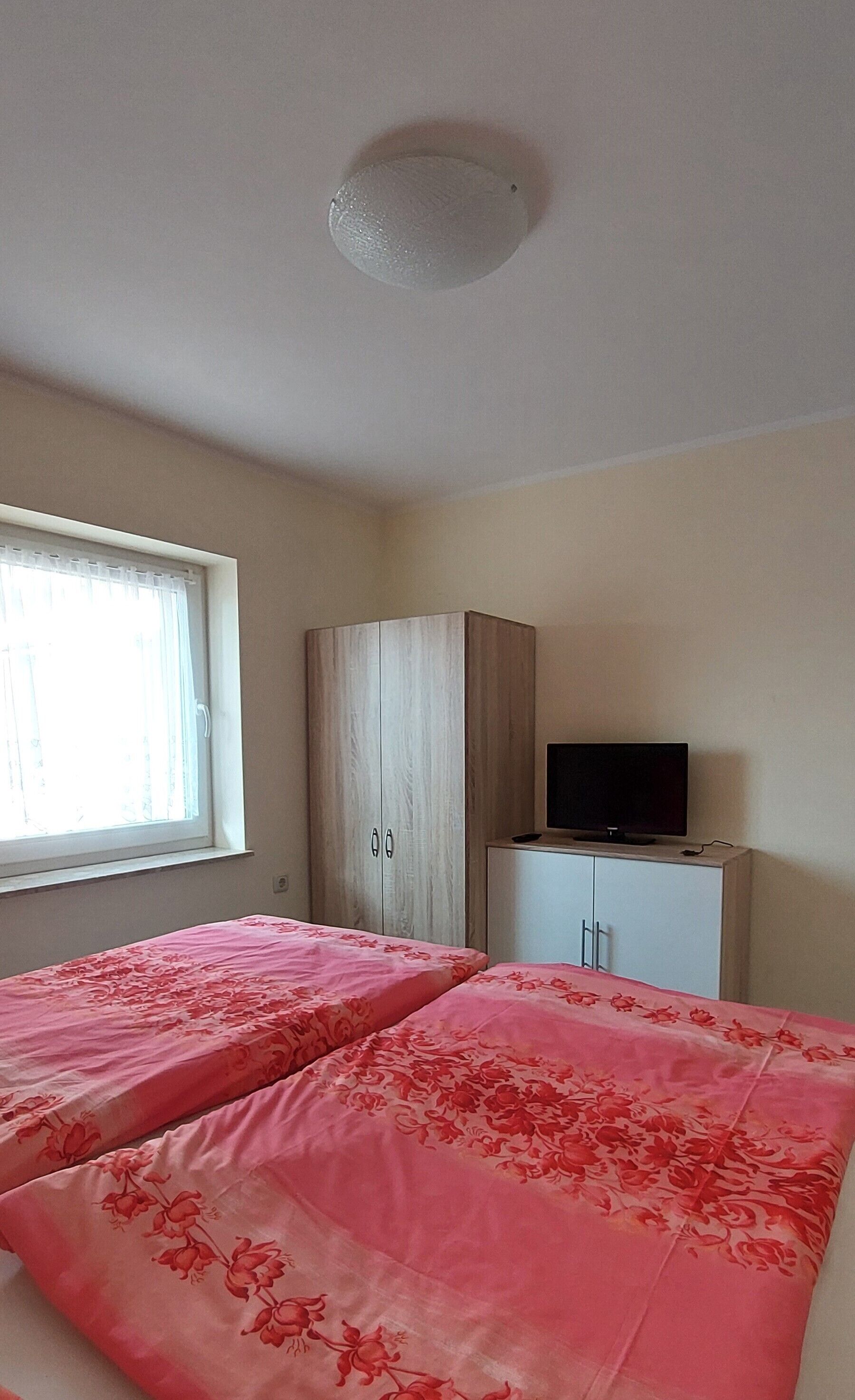A room with two beds, a wardrobe, a television, and a window.