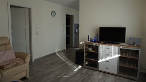 Een woonkamer met een bank, een televisie op een houten kast en een deur naar een andere kamer.
