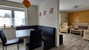 Een woonkamer met een eettafel, zwarte stoelen, een beige bank en een zwarte zitbank.