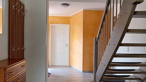 Een gang met een houten vloer, een trap en een deur naar een andere kamer.