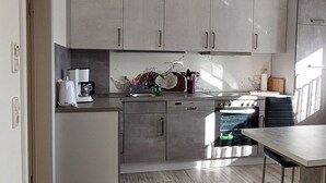 Een moderne keuken met lichte kastjes, een inbouwoven en een eethoek met een tafel en stoelen.