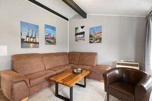 Un salon avec un canapé en cuir marron, une table basse en bois et un fauteuil en cuir marron. Trois tableaux encadrés sont accrochés au mur.