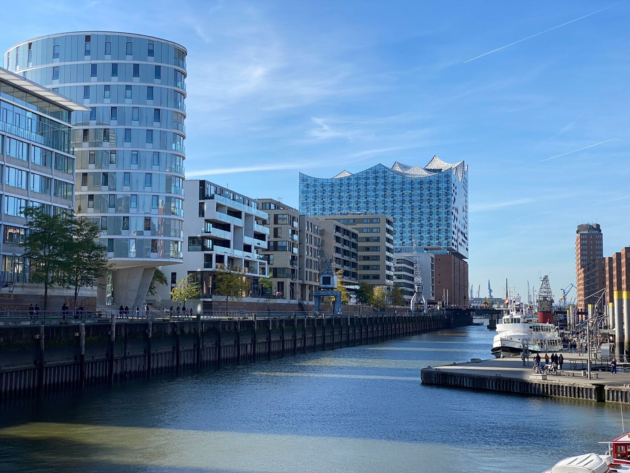 Ein städtisches Ufergebiet mit modernen Gebäuden, einem Fluss und einem Anlegesteg mit Booten.