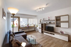A modern living room with a sofa, glass coffee table, TV, and decorative items.