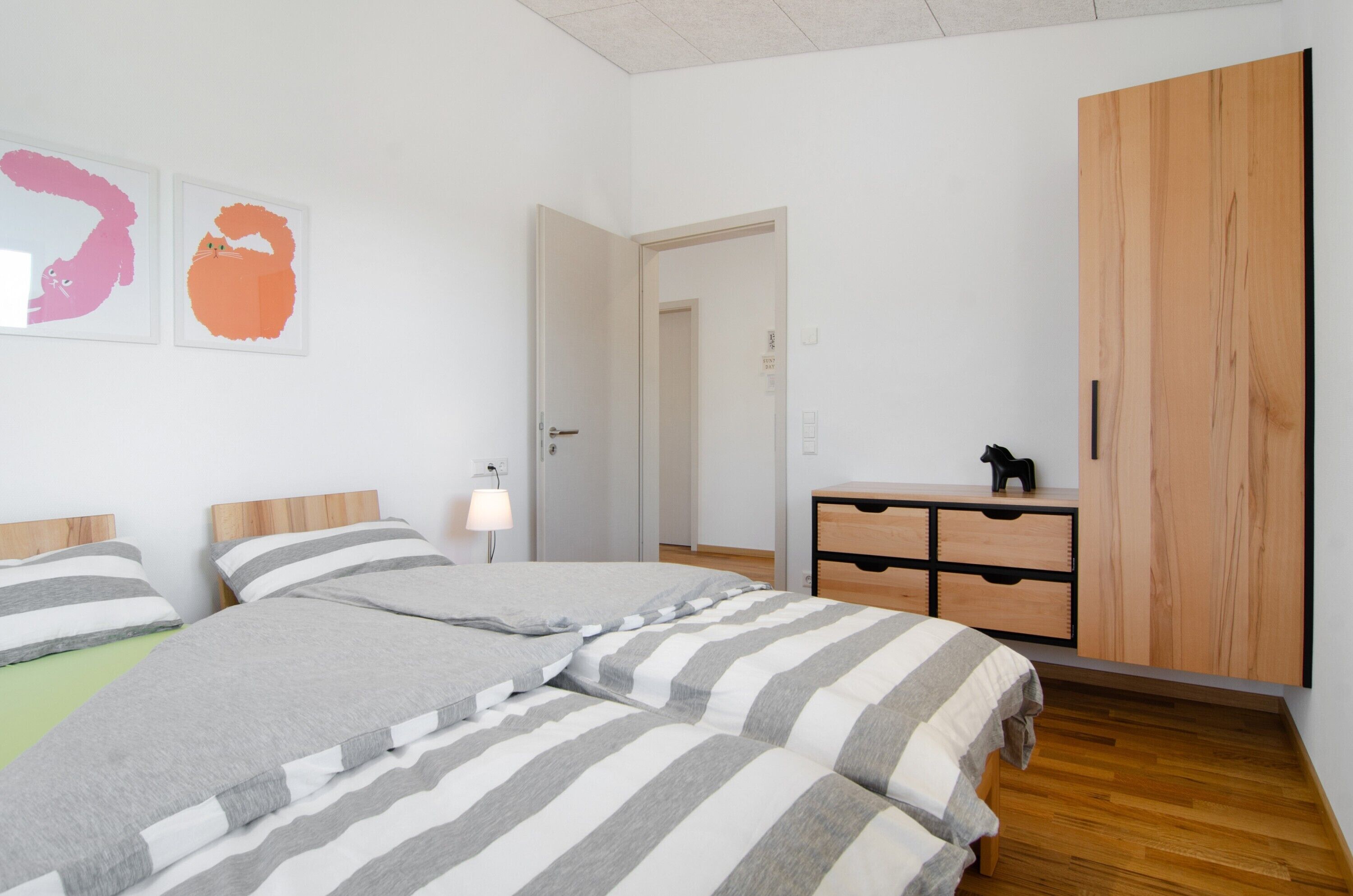 A bedroom with two beds, a wooden dresser, and a door leading to another room.
