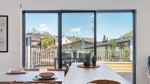 Een eetgedeelte met een lange tafel, stoelen en een uitzicht door grote glazen deuren naar buiten.